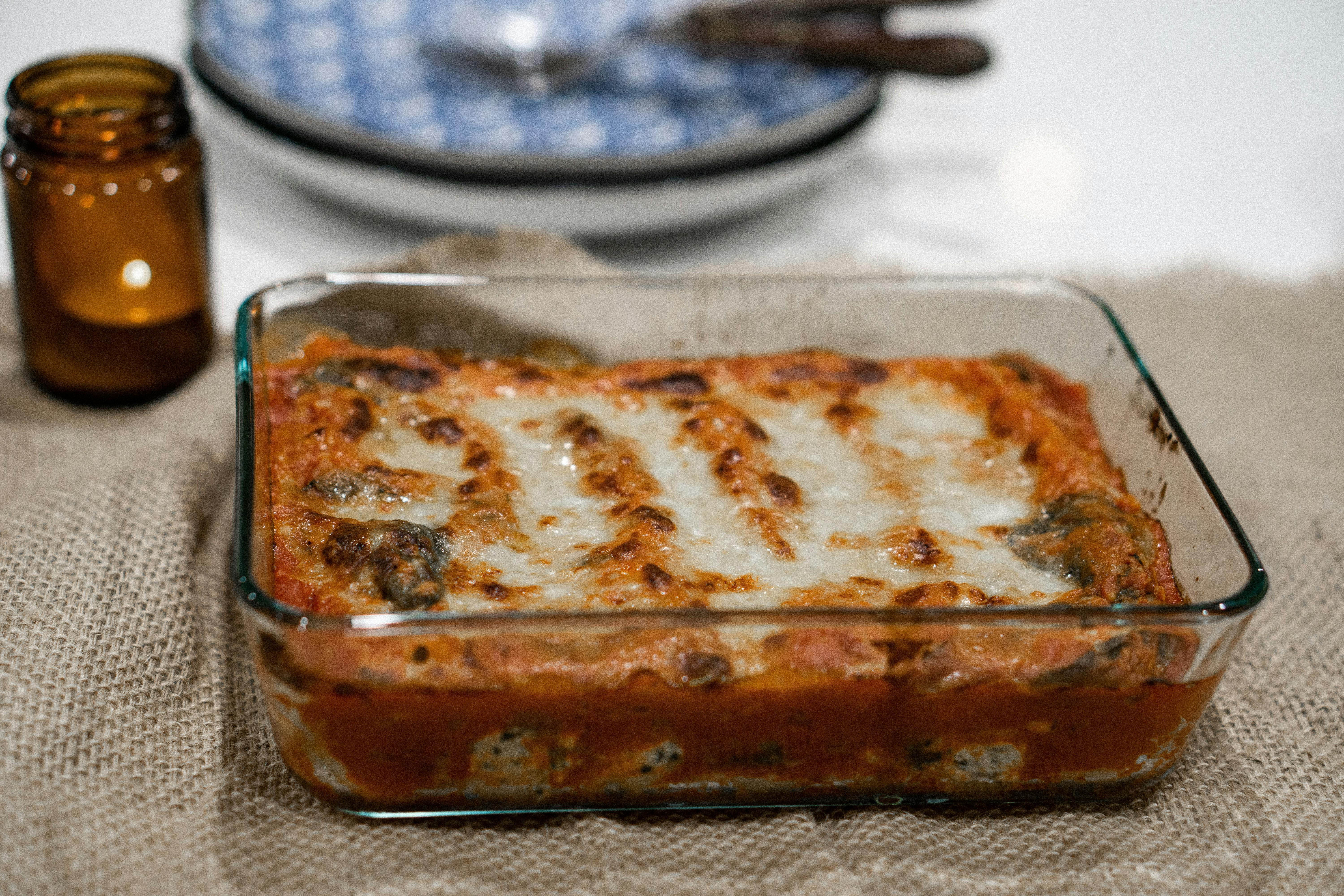 Baked lasagna on a table cloth, candle and plate in the background.